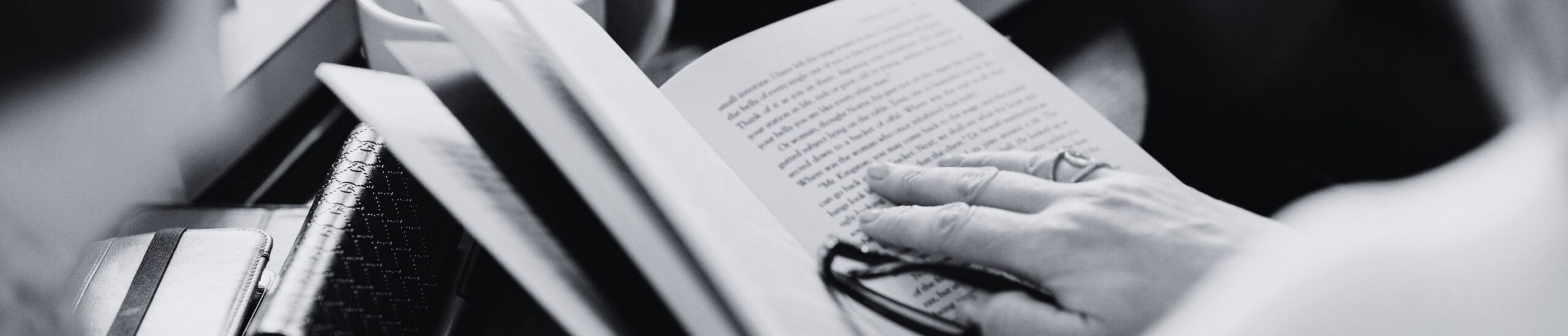 Pessoa imersa na leitura, marcando linha com o dedo e segurando óculos, representando a busca por livros baratos no Portal de Livros.